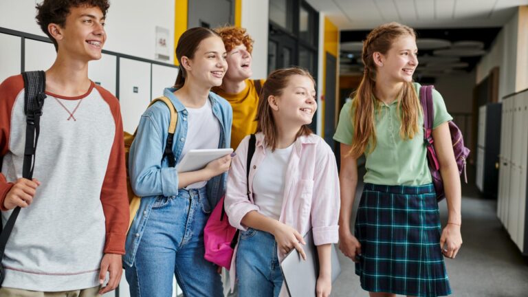 Jugendliche gehen lachend durch den Schulflur an den Spinden vorbei